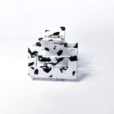 This is a miniature claw clip with a dalmatian print design, featuring irregular black spots on a white background. It has a classic spring-loaded hinge mechanism. The clip's compact size suggests it's ideal for securing smaller sections of hair, half-up styles, or for finer hair types.